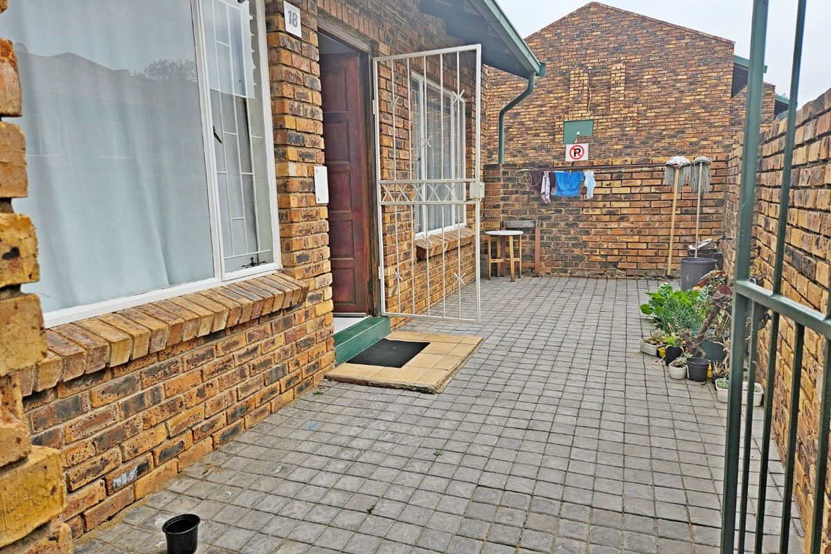 A private paved courtyard area featuring face brick walls, secure gated access, and aluminium window frames, providing a functional outdoor space.