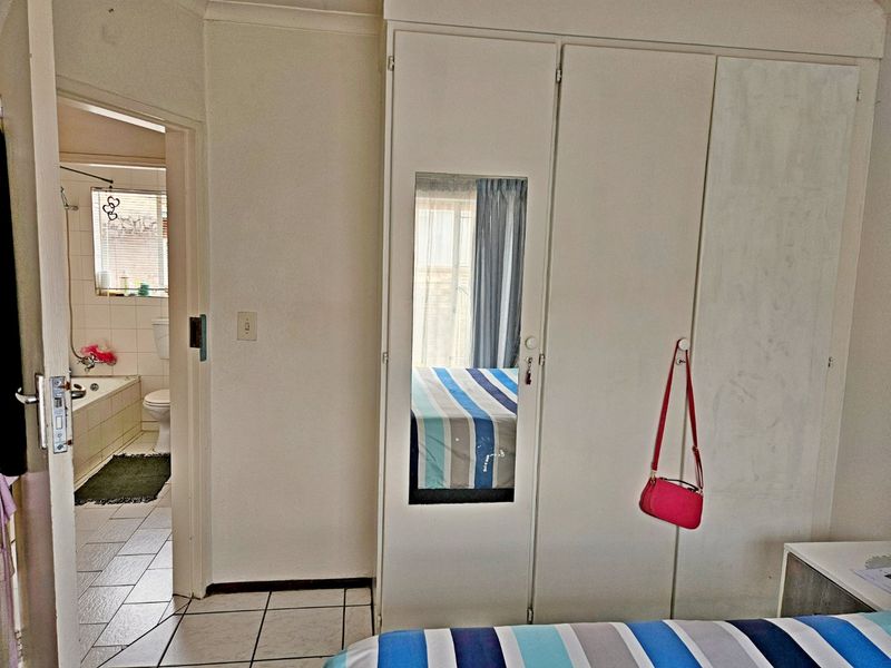 Bedroom featuring built-in cupboards with a mirrored panel and direct access to an en-suite bathroom with tiled flooring.