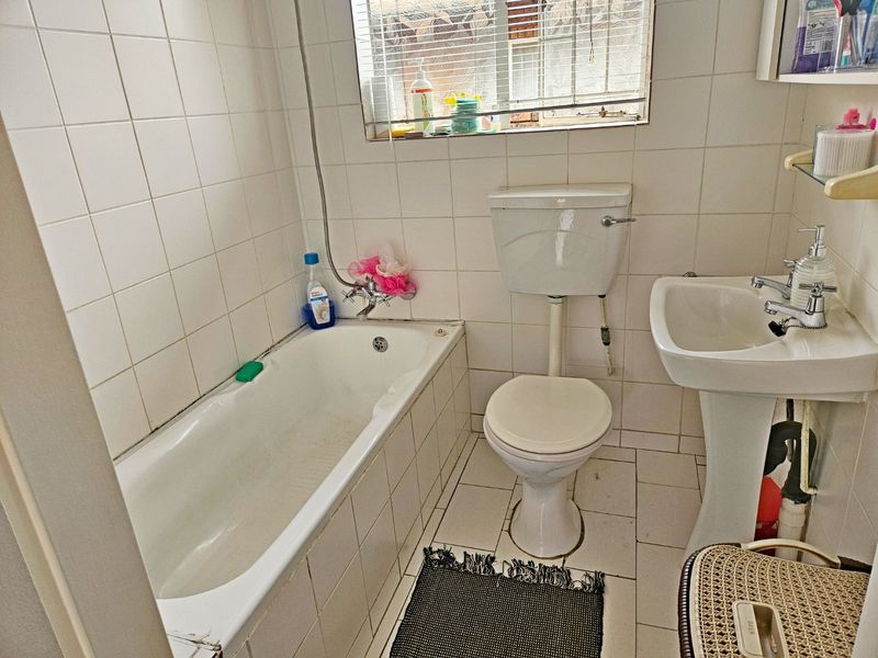 A functional bathroom featuring a bathtub, pedestal basin, and toilet with classic white wall and floor tiling.