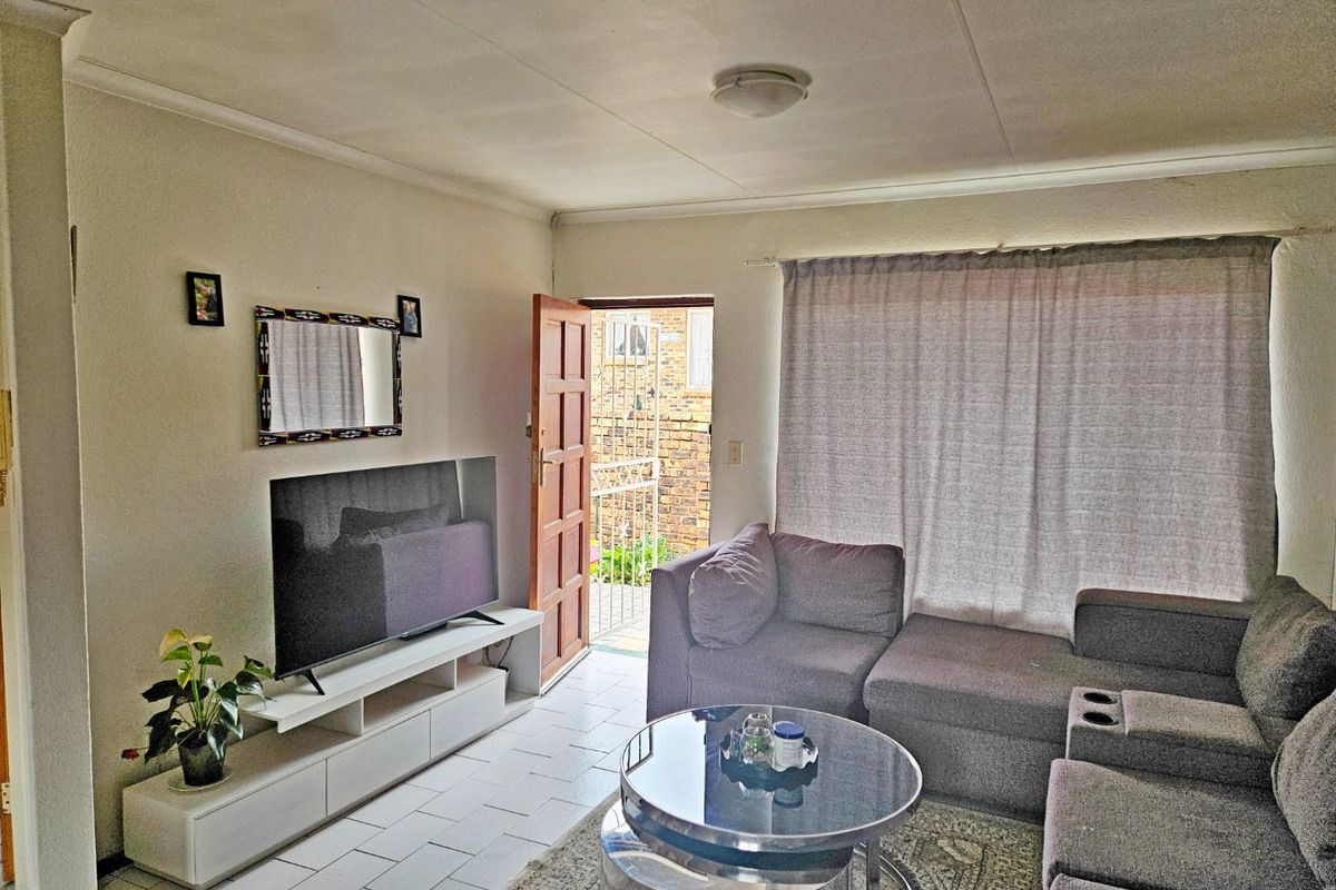 A living room featuring tiled flooring, a ceiling light, and direct access to an exterior entrance with a security gate.