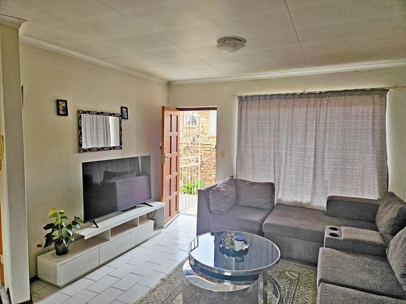 A living room featuring tiled flooring, a ceiling light, and direct access to an exterior entrance with a security gate.