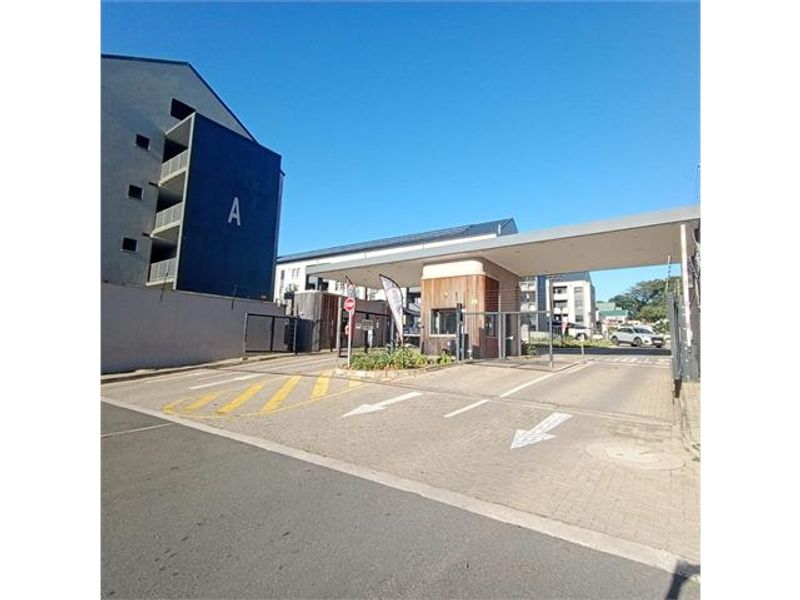The entrance to the apartment complex features a modern security gatehouse, paved driveway, and controlled access point for residents and visitors.