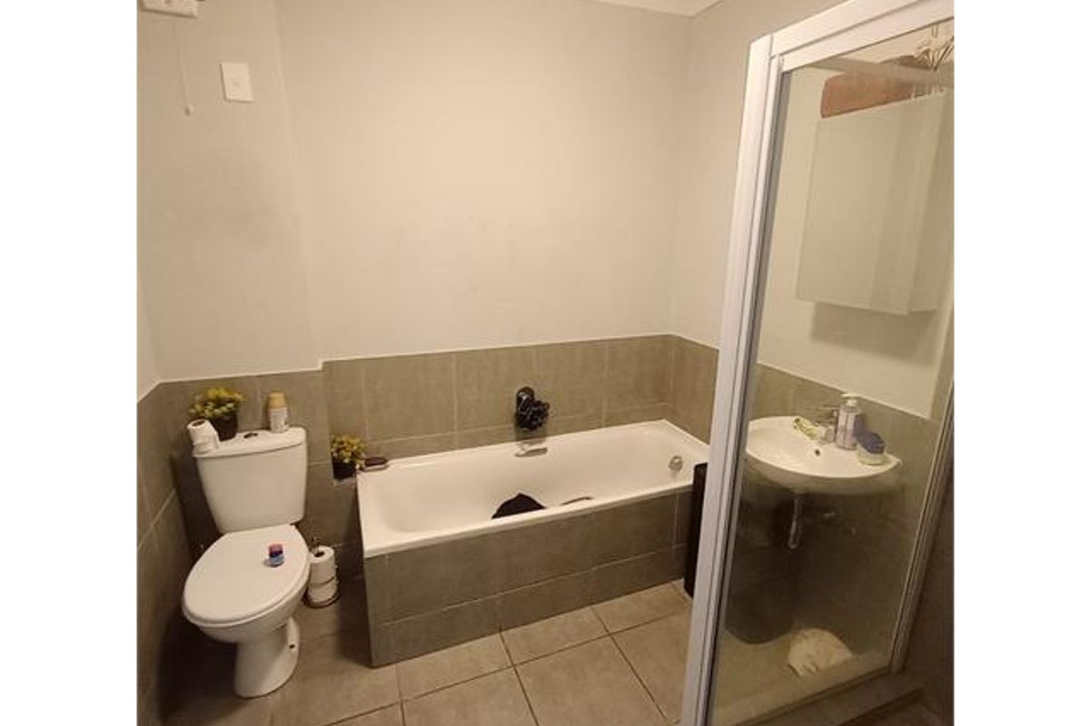 A functional bathroom featuring a bathtub, separate shower enclosure, pedestal sink, and toilet with neutral tiled finishes.