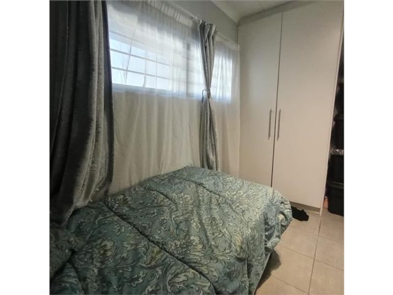A bedroom featuring built-in cupboards, tiled flooring, and security bars on the window.