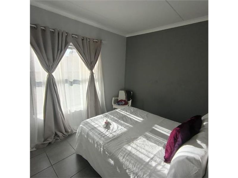 A bedroom featuring tiled flooring, an accent wall, and natural light through window treatments.