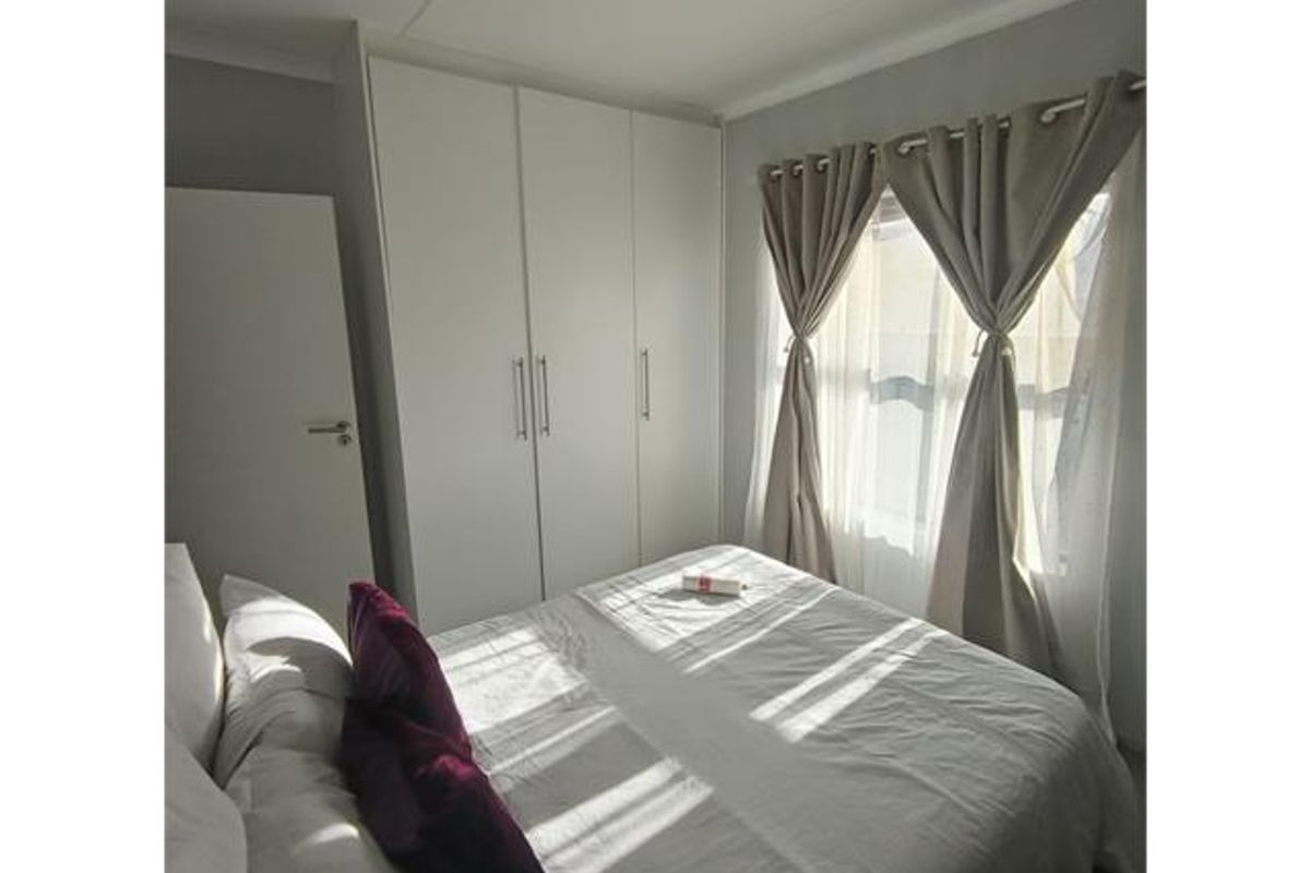 A well-lit bedroom featuring built-in white cupboards and a window with neutral curtains.