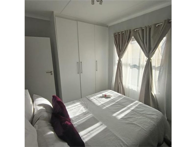 A well-lit bedroom featuring built-in white cupboards and a window with neutral curtains.