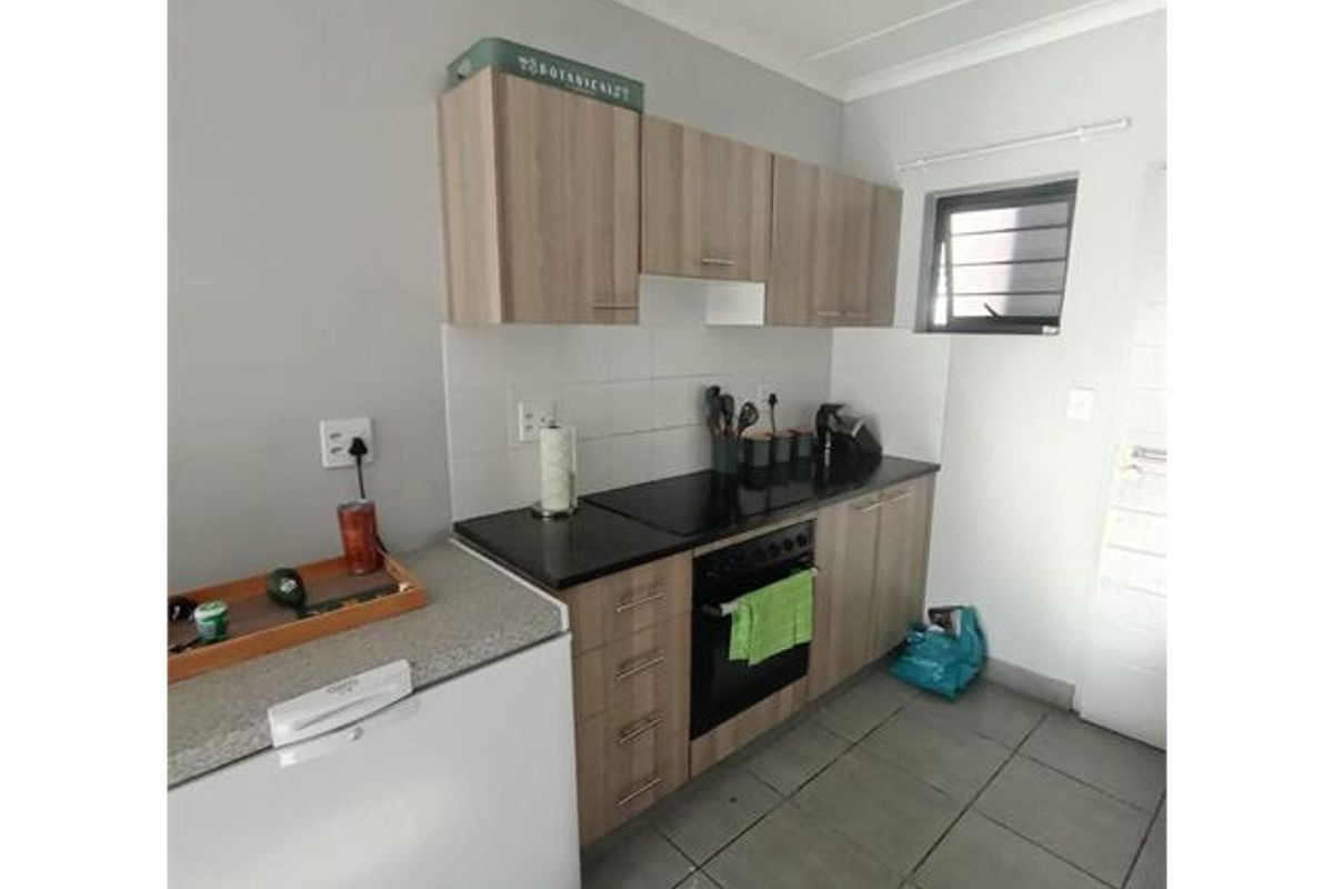 A functional kitchen featuring wood-finish cabinetry, dark countertops, a built-in oven with hob, and tiled flooring.