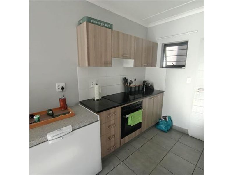 A functional kitchen featuring wood-finish cabinetry, dark countertops, a built-in oven with hob, and tiled flooring.