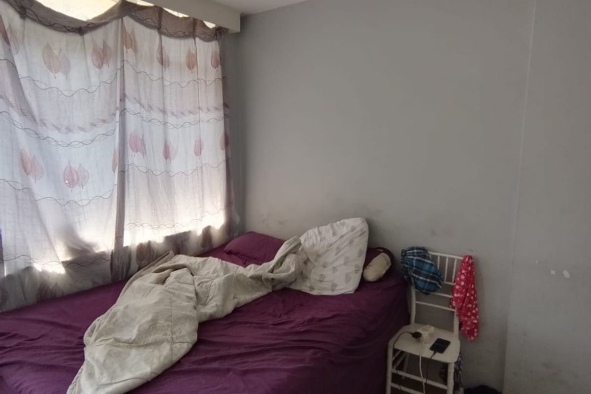 A bedroom featuring laminate flooring and a window with a curtain rail, showing signs of wall wear and staining.