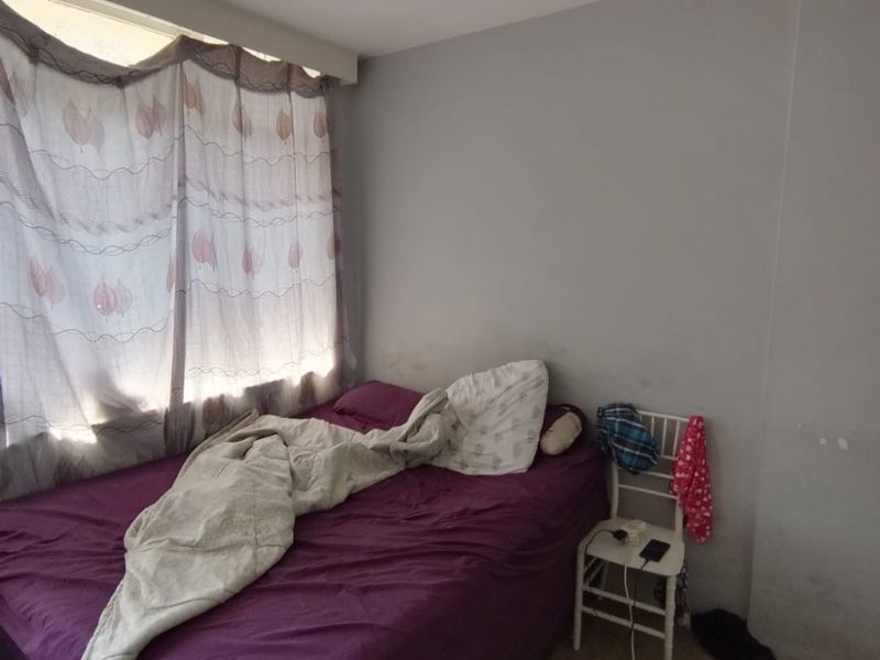 A bedroom featuring laminate flooring and a window with a curtain rail, showing signs of wall wear and staining.