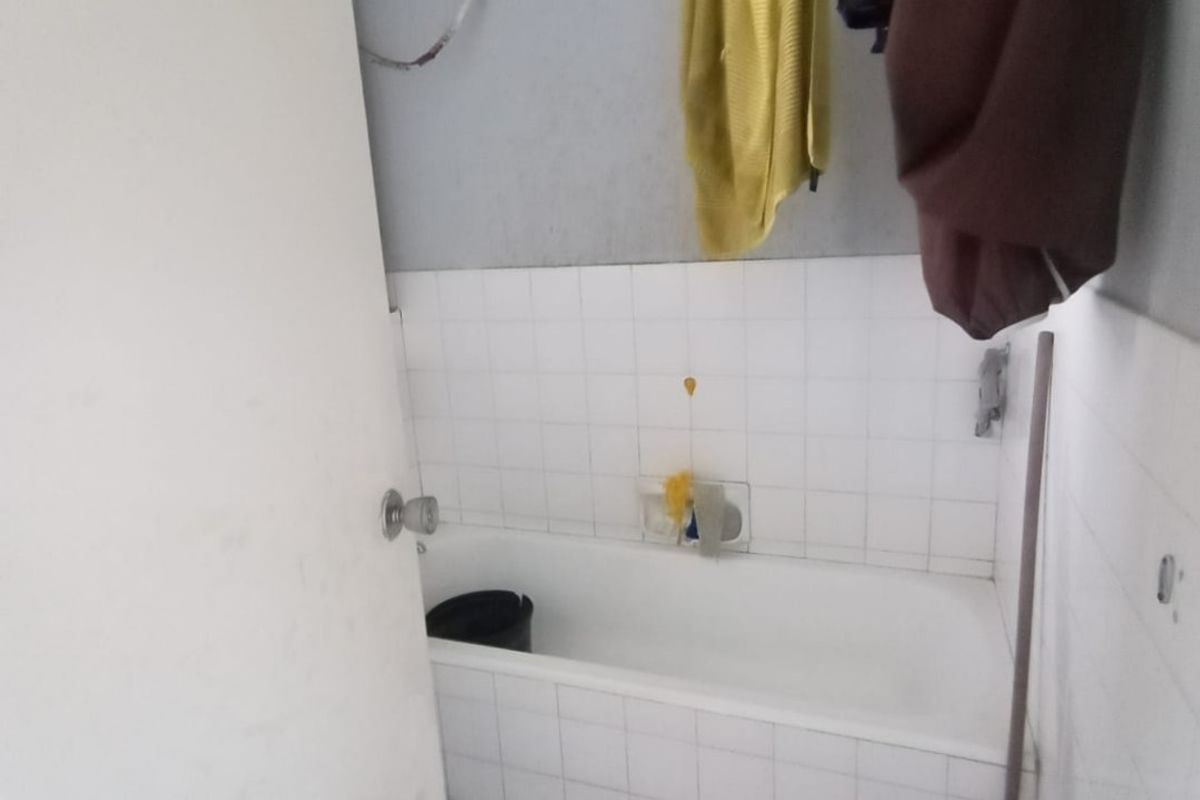 A small bathroom featuring a built-in bathtub with tiled splashback and tiled flooring, requiring cosmetic updates and repairs to wall finishes.