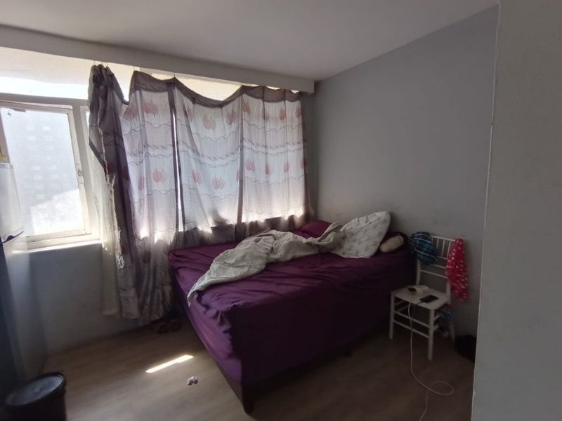 A bedroom featuring laminate flooring and a large window, providing natural light. The space requires cosmetic updates to improve its overall condition.