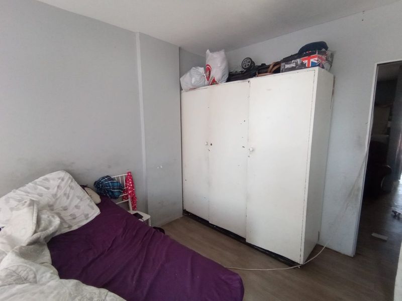 A bedroom featuring laminate flooring and a built-in wardrobe, currently showing signs of wear on the walls.