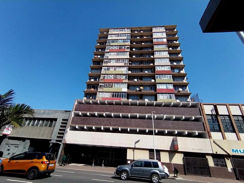 Exterior view of a multi-story apartment building featuring a brick facade, balcony enclosures, and ground-level parking facilities.