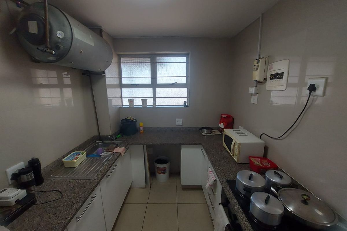 Compact kitchen featuring granite countertops, built-in cabinetry, an electric hob, and a wall-mounted water heater with tiled finishes throughout.