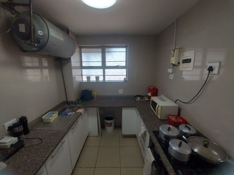 Compact kitchen featuring granite countertops, built-in cabinetry, an electric hob, and a wall-mounted water heater with tiled finishes throughout.