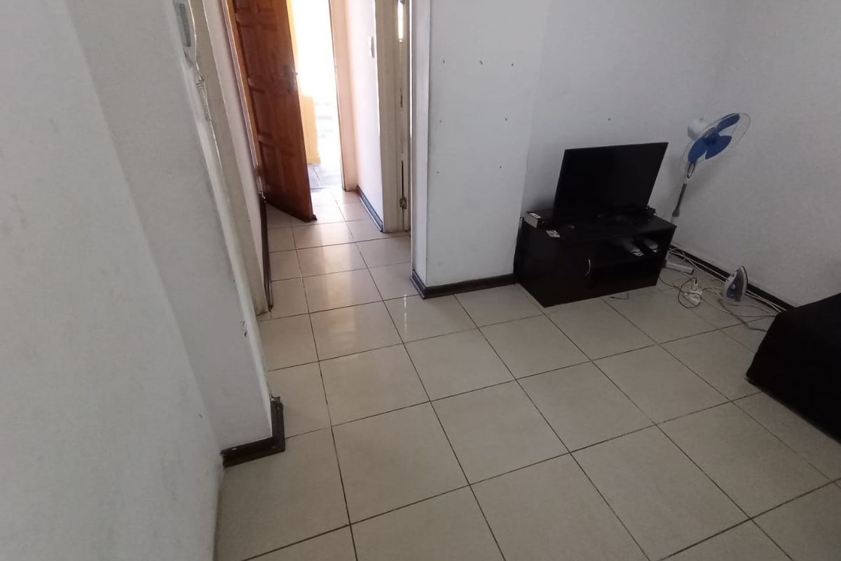 A compact living area featuring neutral tiled flooring and an intercom system, showing signs of wear on the walls and skirting boards.