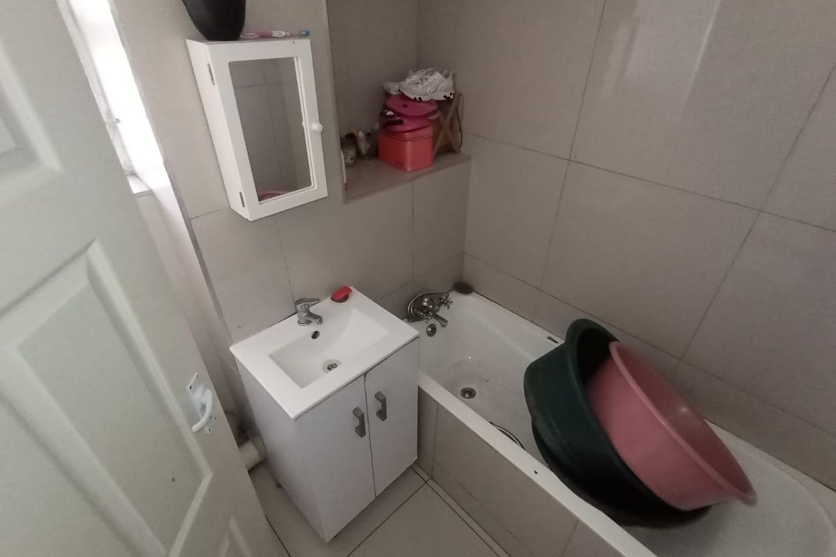 A compact bathroom featuring a built-in vanity with basin, a standard bathtub, and neutral wall and floor tiling.