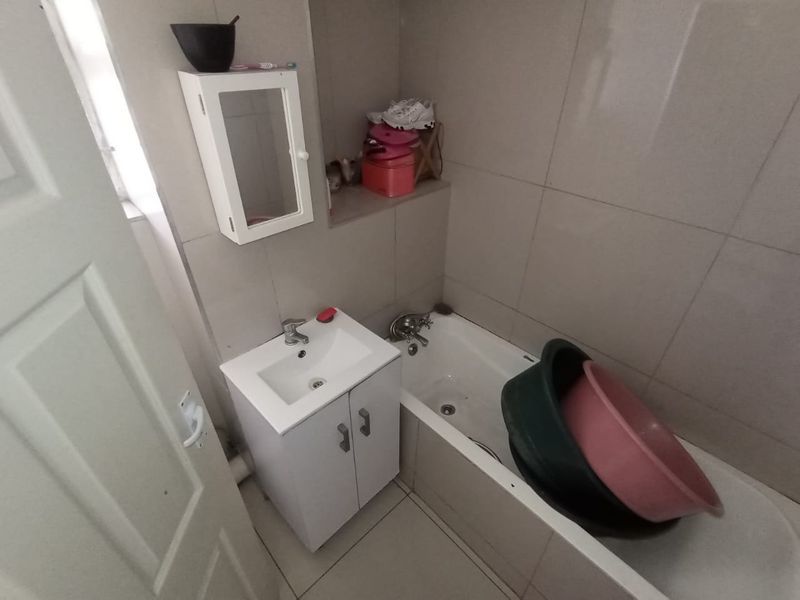 A compact bathroom featuring a built-in vanity with basin, a standard bathtub, and neutral wall and floor tiling.