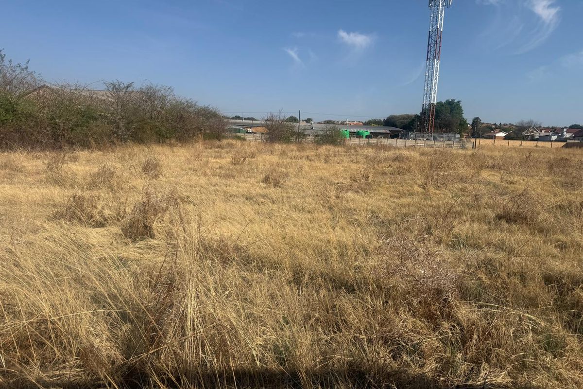 A view of a vacant residential plot featuring dry grass and a telecommunications tower in the background.