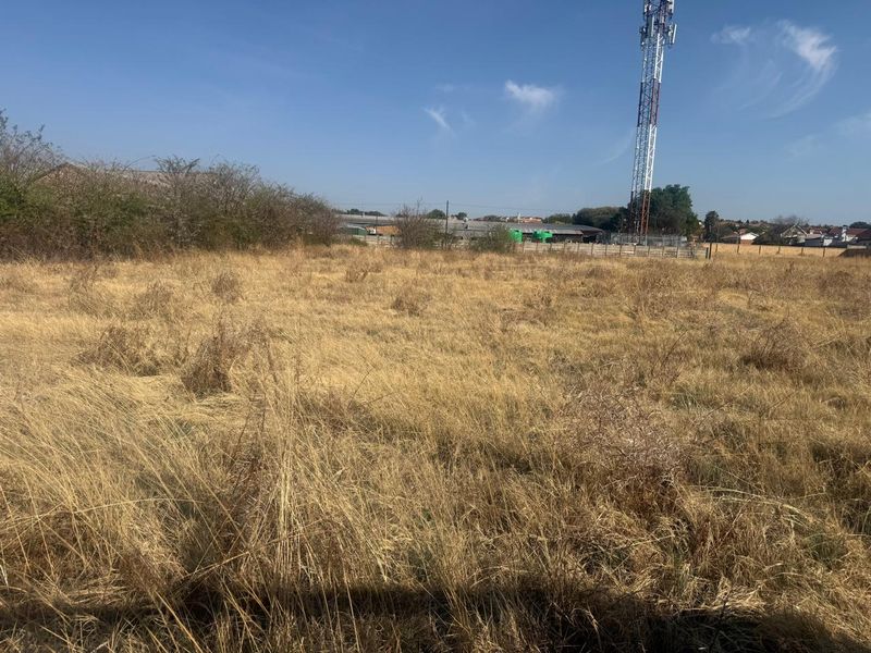A view of a vacant residential plot featuring dry grass and a telecommunications tower in the background.