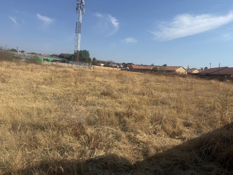 A vacant residential plot featuring dry grass and a prominent telecommunications tower in the background.