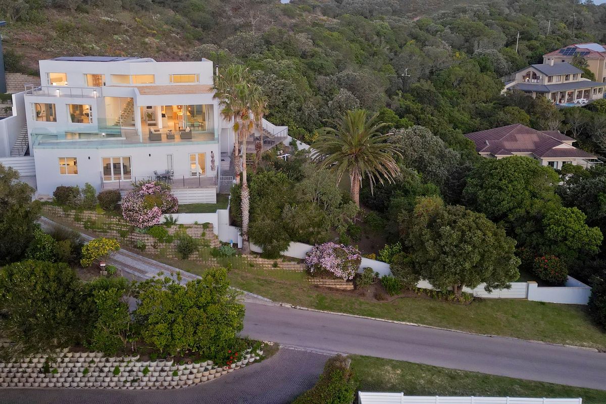 Aerial view of a modern multi-level residence featuring glass balustrades, solar panels, and landscaped terraced gardens set against a lush hillside.