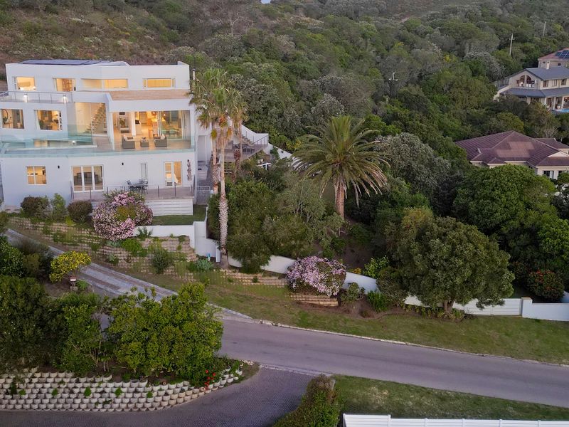 Aerial view of a modern multi-level residence featuring glass balustrades, solar panels, and landscaped terraced gardens set against a lush hillside.