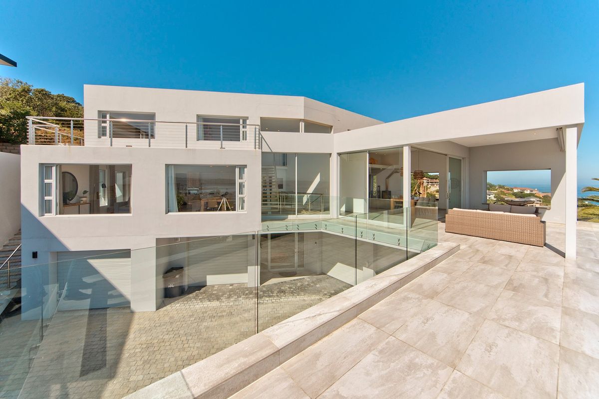Modern multi-level residence featuring a spacious tiled patio, glass balustrades, and a paved driveway with integrated garage access.