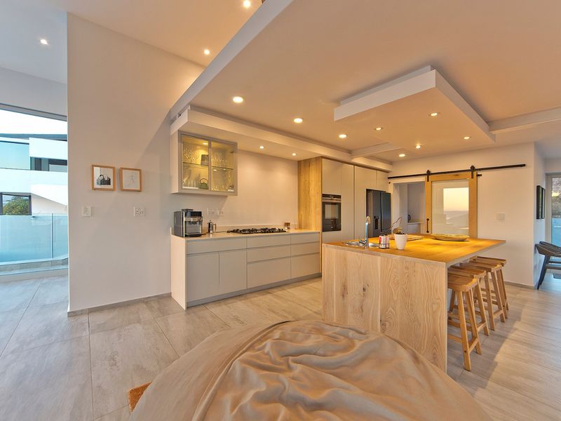 Modern open-plan kitchen featuring sleek cabinetry, a large wooden island, integrated appliances, and recessed lighting, seamlessly connecting to the outdoor living area.