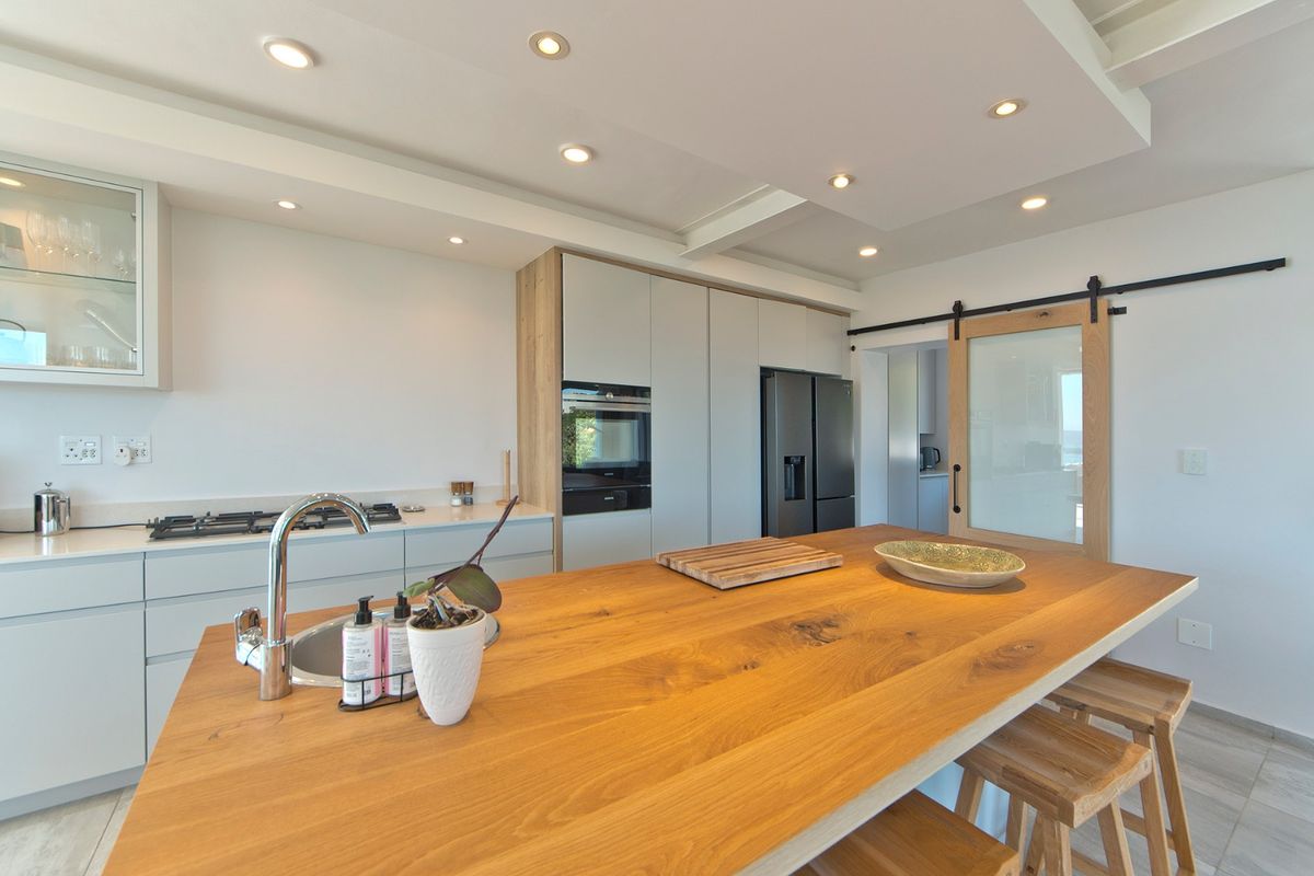 Modern kitchen featuring a large wooden island, integrated appliances, sleek cabinetry, recessed lighting, and a sliding barn door leading to a secondary space.
