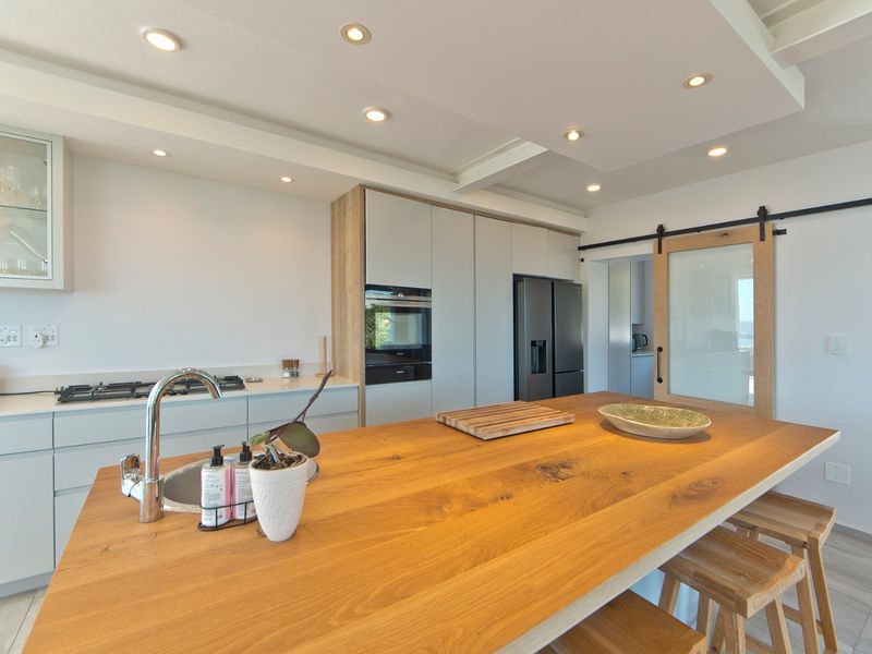 Modern kitchen featuring a large wooden island, integrated appliances, sleek cabinetry, recessed lighting, and a sliding barn door leading to a secondary space.