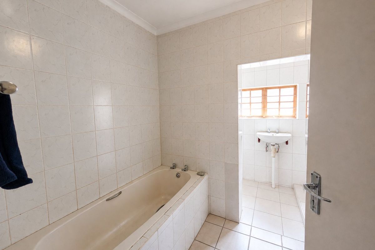 A functional bathroom featuring a built-in bathtub and a separate basin area with tiled finishes throughout.
