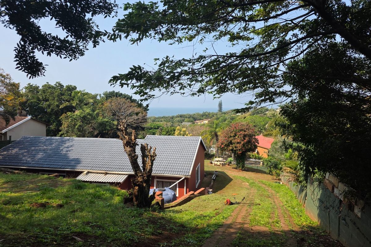 Rear view of the property featuring a tiled roof, rainwater tank, and a sloping garden with a distant ocean view.