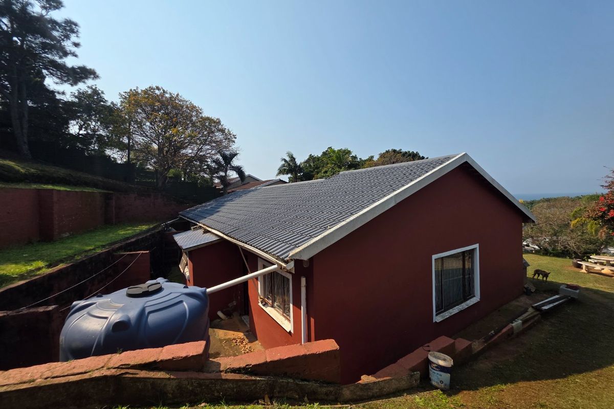 Rear view of the house featuring a tiled roof, exterior water storage tank, and surrounding retaining walls on a sloped garden plot.