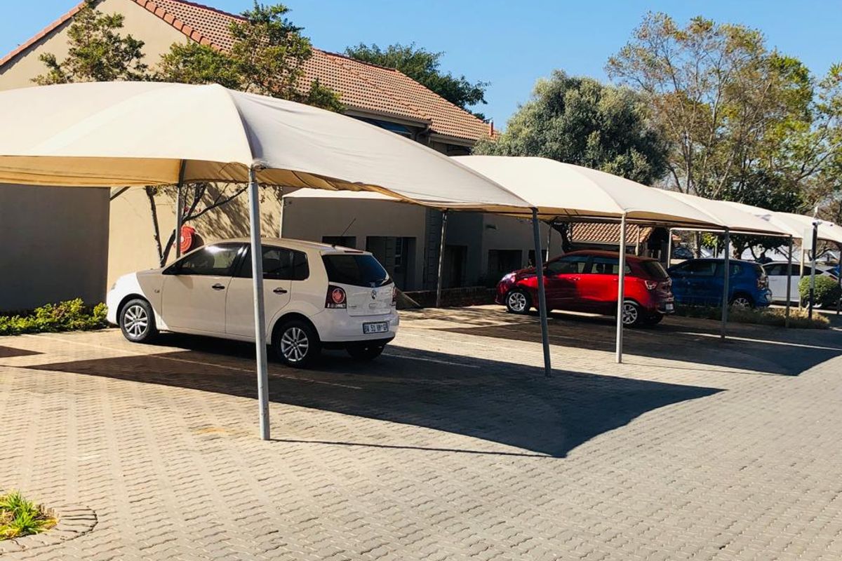 Outdoor parking area featuring multiple shade cloth carports over a paved driveway surface.