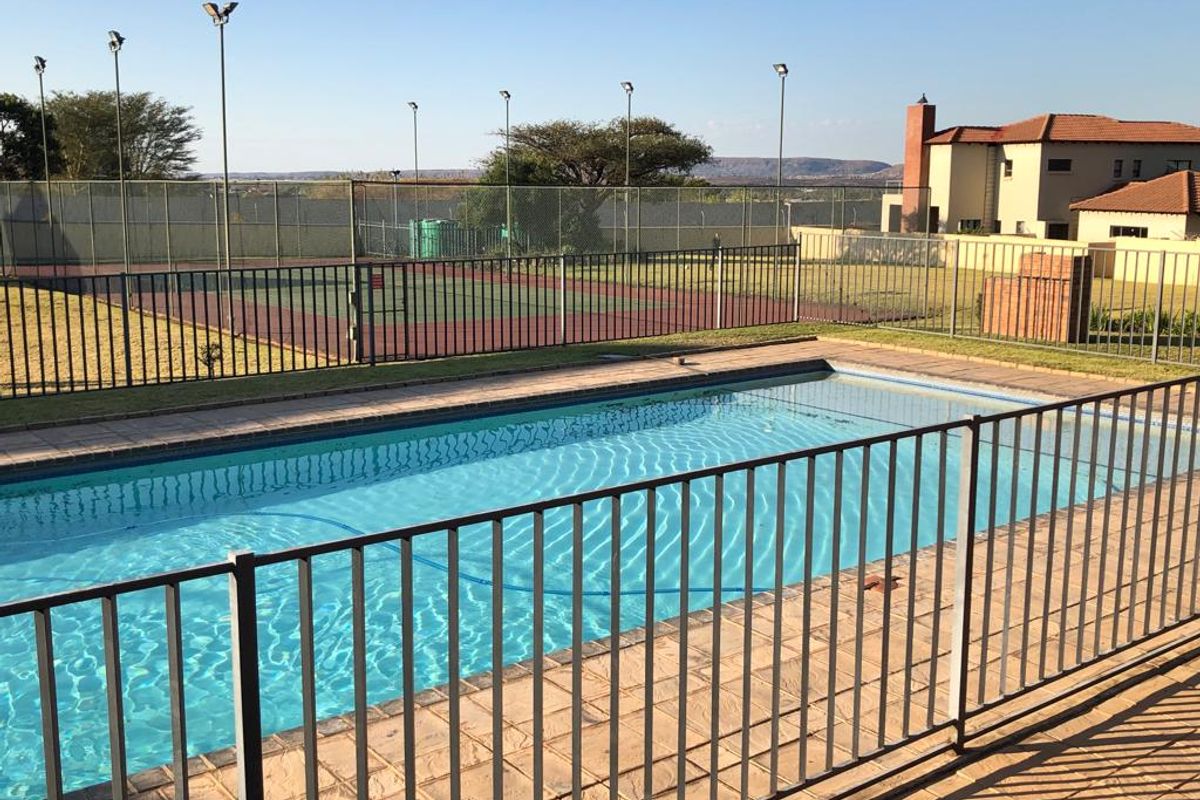 Communal outdoor area featuring a swimming pool with safety fencing and an adjacent tennis court with floodlights.