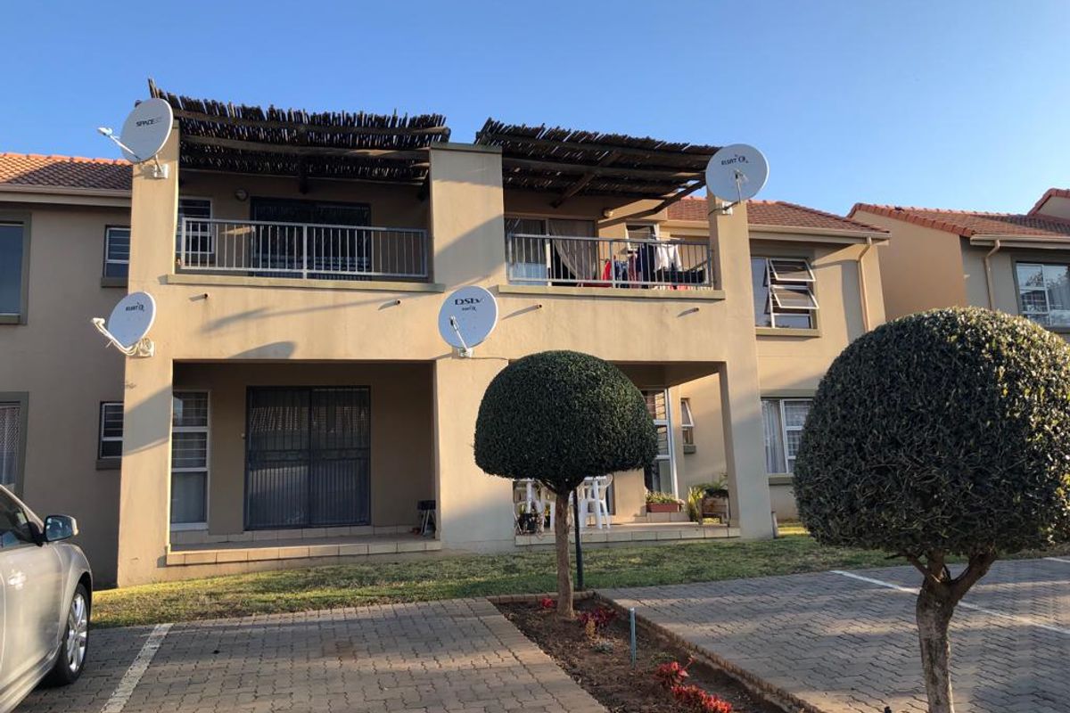 Front elevation of a two-story apartment complex featuring paved parking, ground floor patios, and upper-level balconies with thatched roof coverings.