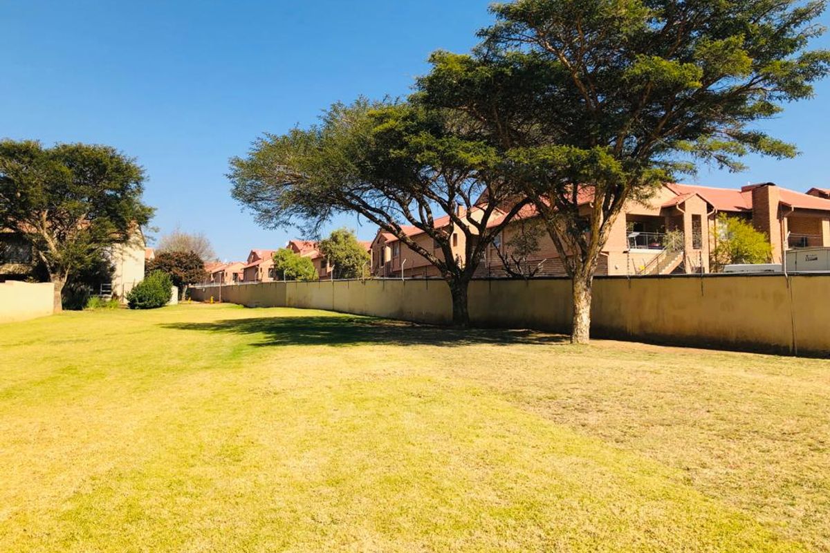 A spacious communal garden area featuring established trees and a perimeter wall within a residential apartment complex.