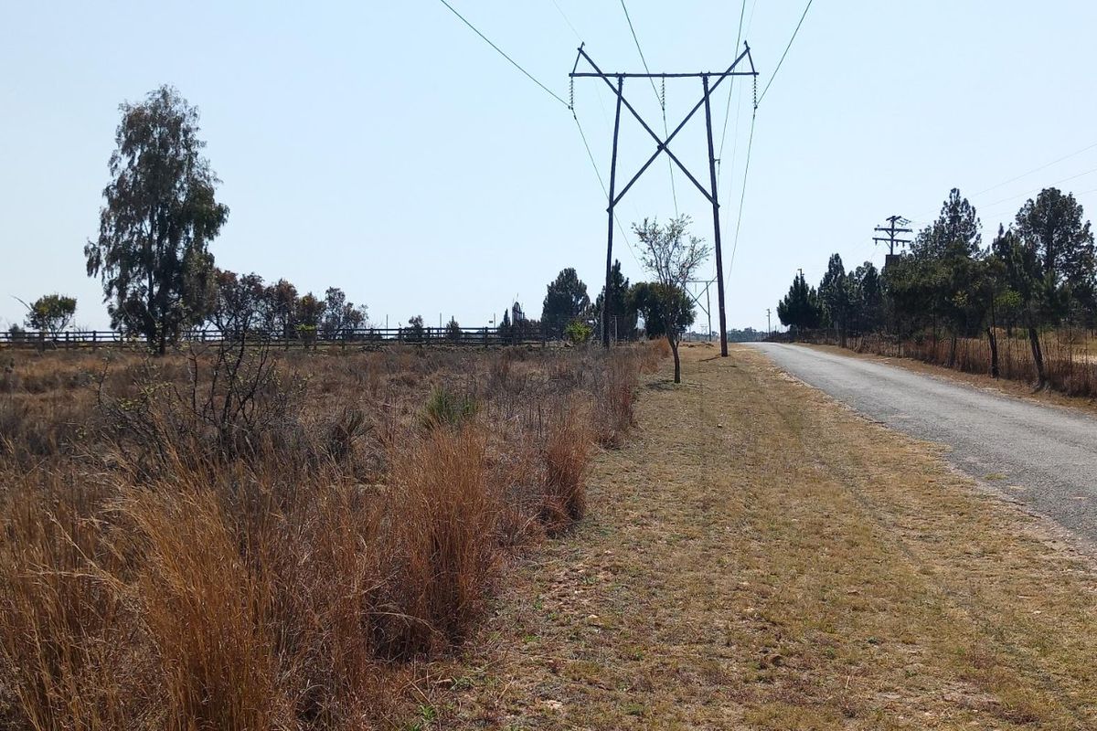 A view of the vacant residential land adjacent to a paved road, featuring overhead power lines and perimeter fencing.
