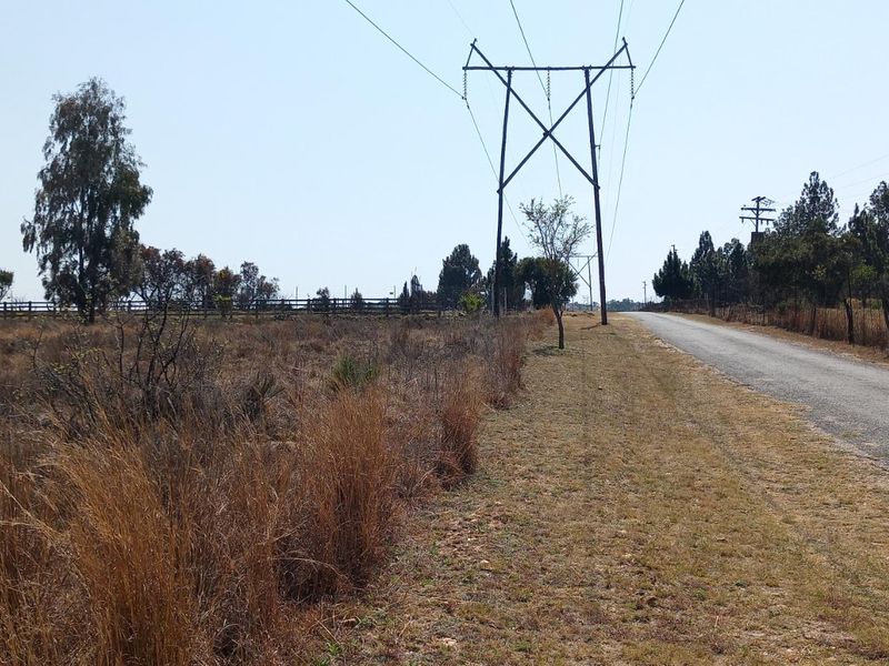 A view of the vacant residential land adjacent to a paved road, featuring overhead power lines and perimeter fencing.