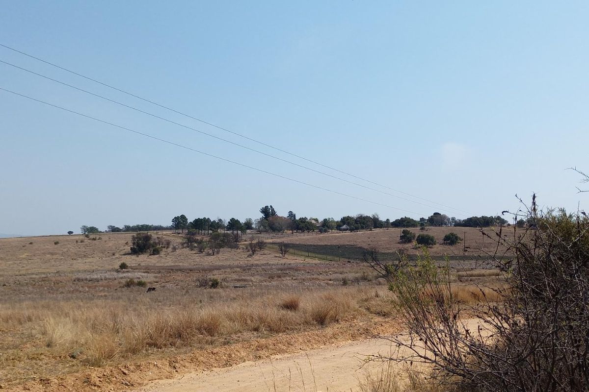 A wide-angle view of vacant residential land featuring a dirt access road, wire fencing, and overhead power lines across the landscape.