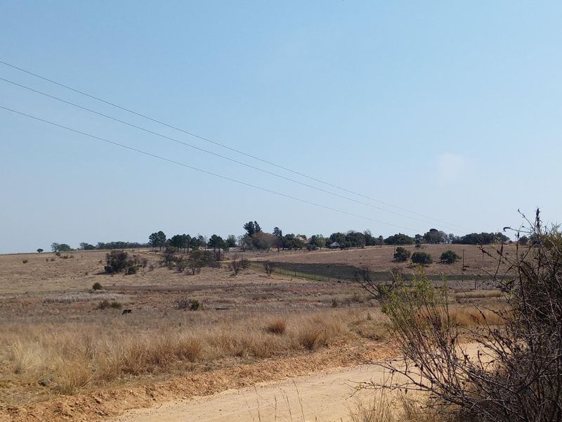 A wide-angle view of vacant residential land featuring a dirt access road, wire fencing, and overhead power lines across the landscape.