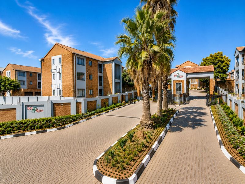 The entrance to Bel Aire apartment complex featuring a paved driveway, security gatehouse, and well-maintained brick building facades.