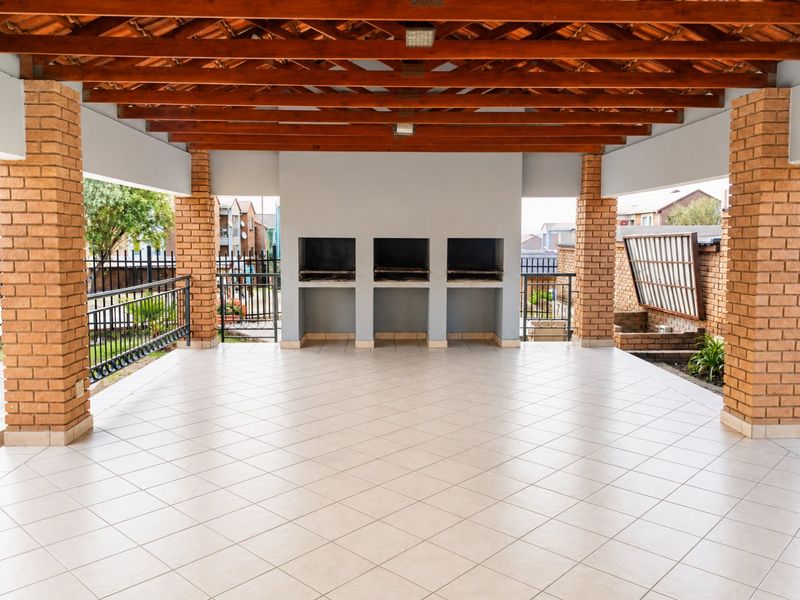 Spacious covered patio featuring a tiled floor, exposed timber beams, brick pillars, and a built-in triple braai area, perfect for outdoor entertaining.