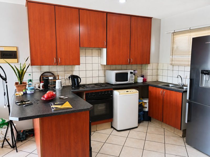 Functional kitchen featuring wood-look laminate cabinetry, dark countertops, tiled backsplash, built-in oven, and a double basin sink with tiled flooring.