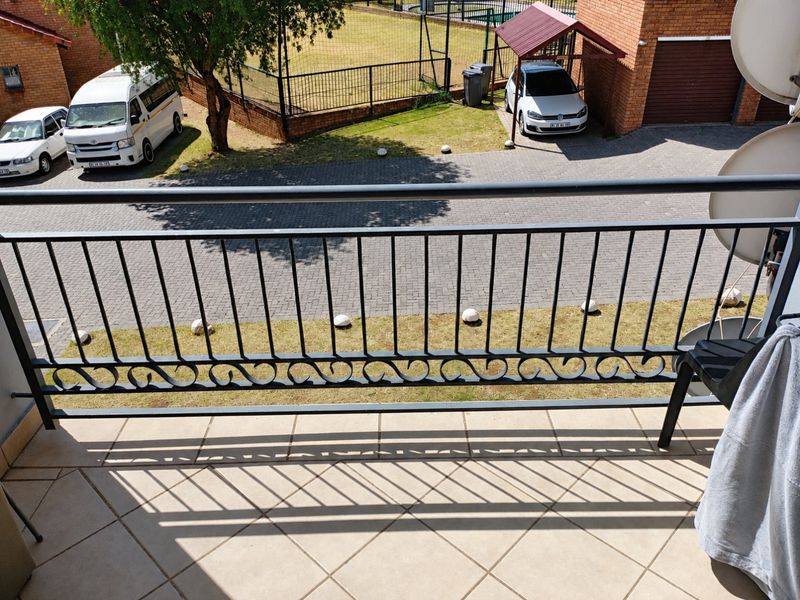 A balcony featuring tiled flooring and a decorative metal balustrade, overlooking the complex parking area and grounds.