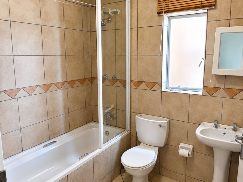 A functional bathroom featuring a bathtub with a glass shower screen, pedestal basin, and toilet, finished with neutral wall and floor tiling.