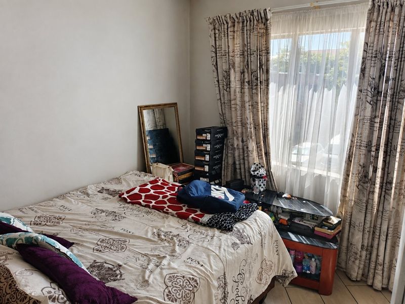 A bedroom featuring tiled flooring and a large window with curtains, providing natural light to the space.
